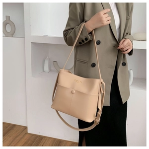 Close-up of beige leather shoulder bag with decorative buckle and gold text on a model