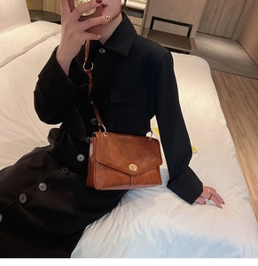 Close-up of caramel brown leather shoulder bag with gold circular metal clasp detail