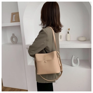 Detail of minimalist beige bucket bag with front pocket and gold Classic Bag logo