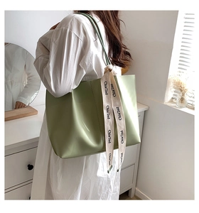 Close-up of a large pale green tote bag with ribbon detail worn by a model in a room