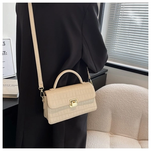 Close-up of beige crocodile pattern handbag with gold clasp on a model in home setting