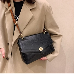 Detail of vintage black textured leather crossbody bag with golden twist lock and brown strap