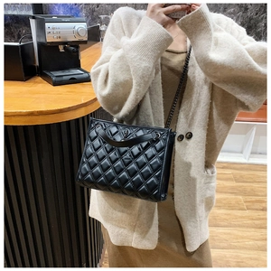 Close-up of black quilted shoulder bag featuring metal chain strap and leather handle
