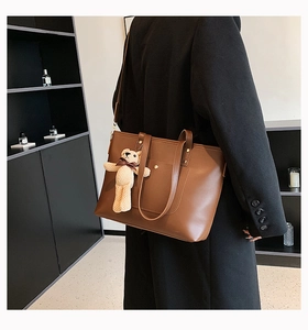 Brown leather tote bag detail with beige knitted bear charm and decorative front pocket