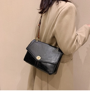 Close-up of black retro textured shoulder bag with a gold metal clasp worn by a model