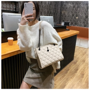 Close-up of beige quilted crossbody bag with metal chain strap and luxury diamond stitching