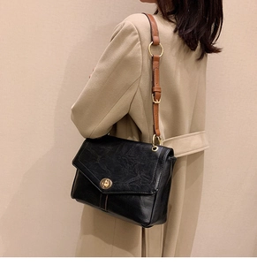 Detail of vintage black leather crossbody bag with golden rotary lock and brown strap