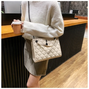 Chic beige quilted tote bag with chain strap shown in a lifestyle cafe setting