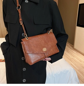 Retro brown crossbody bag with gold buckle detail shown on black coat with leather texture