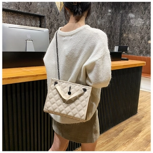Detail of cream quilted shoulder bag with black metal chain and round charm