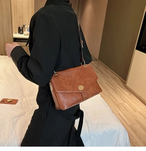 Close-up of a vintage brown crossbody bag with gold buckle worn by a model in black outfit