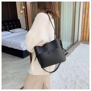 Detail of a black bucket bag with Classic Bag gold lettering worn by a model