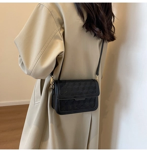 Detail view of a black 3D cube embossed crossbody bag worn with a beige trench coat