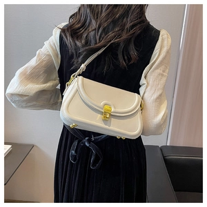 Detail view of cream leather shoulder bag with gold hardware worn by model in minimalist setting