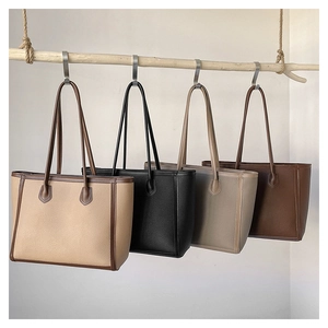 Detail of four large minimalist tote bags in various colors hanging on a wooden rod