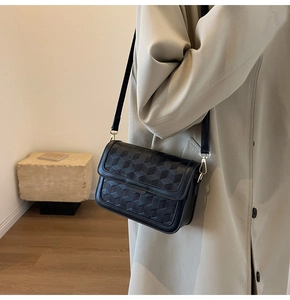 Detail of a black crossbody bag with geometric woven texture and gold metal hooks