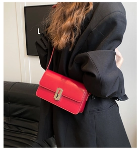 Close-up of a red leather saddle bag with silver metallic clasp worn by a model