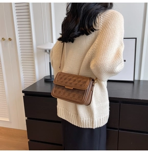 Detail of brown crossbody bag featuring geometric embossed pattern and metal bar closure