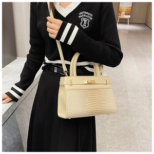 Close-up of beige crocodile embossed handbag featuring golden twist lock and sleek texture
