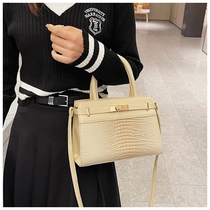 Detail of cream faux leather handbag featuring crocodile pattern texture and gold twist lock