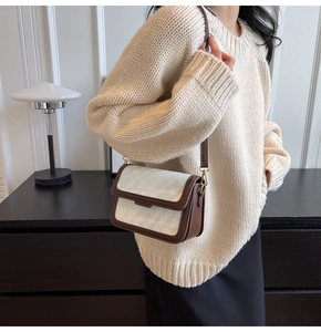 Detail of a chic geometric textured crossbody bag worn over a beige sweater in a cozy setting