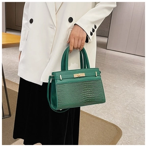 Detail of dark green crocodile texture handbag with gold hardware lock and leather handles