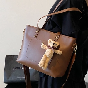 Brown leather tote bag with a knit bear charm and front pocket shown on shoulder