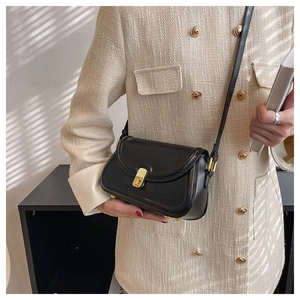 Close-up of black leather crossbody bag with a textured gold rectangular clasp on a tweed jacket