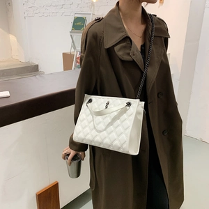 White quilted crossbody bag with chain strap worn with a stylish brown coat