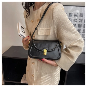 Detail of a black leather shoulder bag with a gold metal twist-lock on a tweed jacket