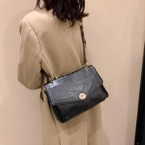 Retro black crossbody bag with pleated texture and gold lock worn with a beige coat