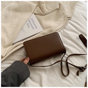 Detail view of the dark brown leather saddle bag held by hand in a minimalist setting