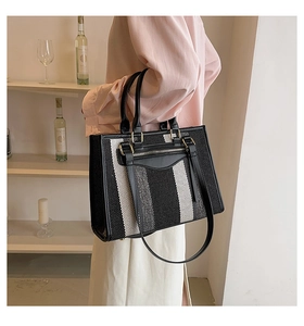 Detail van gestreepte canvas tas met zwart lederen bies en ritsvak gedragen door een model