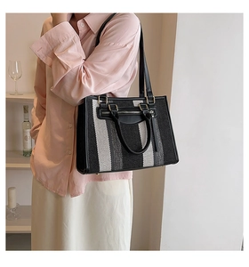 Detail of striped canvas tote bag with black leather trim and gold zipper accents