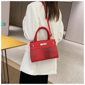 Detail of red crocodile texture structured handbag featuring golden metal turn-lock closure