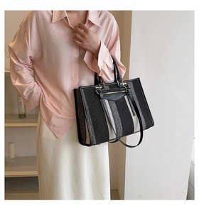 Detail van canvas tote bag met zwart-witte strepen, lederen handvatten en metalen hardware