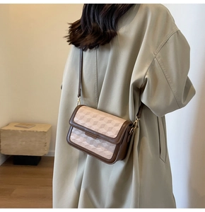 Detail of crossbody box bag with geometric pattern worn by a model in a trench coat