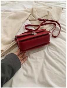 Close-up of red leather saddle bag with silver square buckle on white fabric