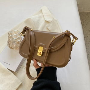 Close-up of tan leather crossbody bag featuring a gold twist lock and rivet details