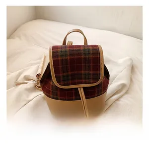 Detail of red and green plaid fabric and brown leather handle on a mini backpack