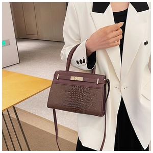 Detail of burgundy crocodile texture leather and golden turn-lock on structured handbag