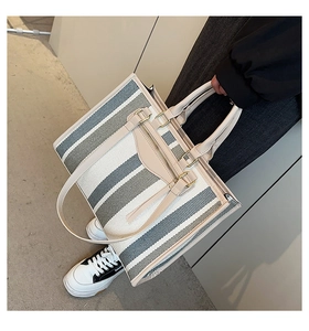 Detail view of large canvas tote bag featuring contrast stripes and cream leather handles