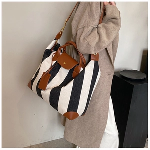 Détail du sac cabas en toile rayée avec anses en cuir porté par un mannequin en manteau