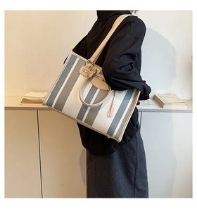 Detail view of large striped canvas tote bag with leather straps and front zip pocket