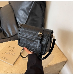Detail of black geometric embossed leather shoulder bag with adjustable gold buckle strap