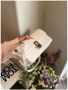 Close-up of white saddle bag with silver metal buckle on a minimalist magazine backdrop