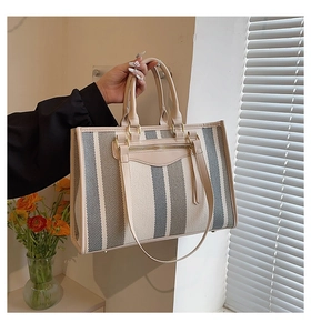 Detailed close-up of striped canvas tote bag with leather straps and gold metal rings