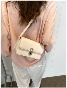 Side view of a minimalist cream saddle bag with silver buckle worn by a model