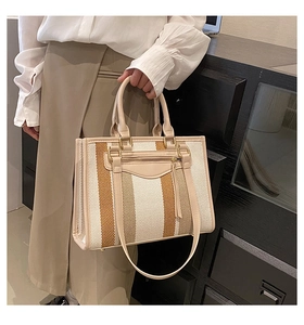 Detail of canvas tote bag showing striped pattern, leather handles, and external zip pocket