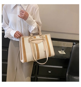 Model showing a large striped canvas tote bag with beige leather trim and tassels